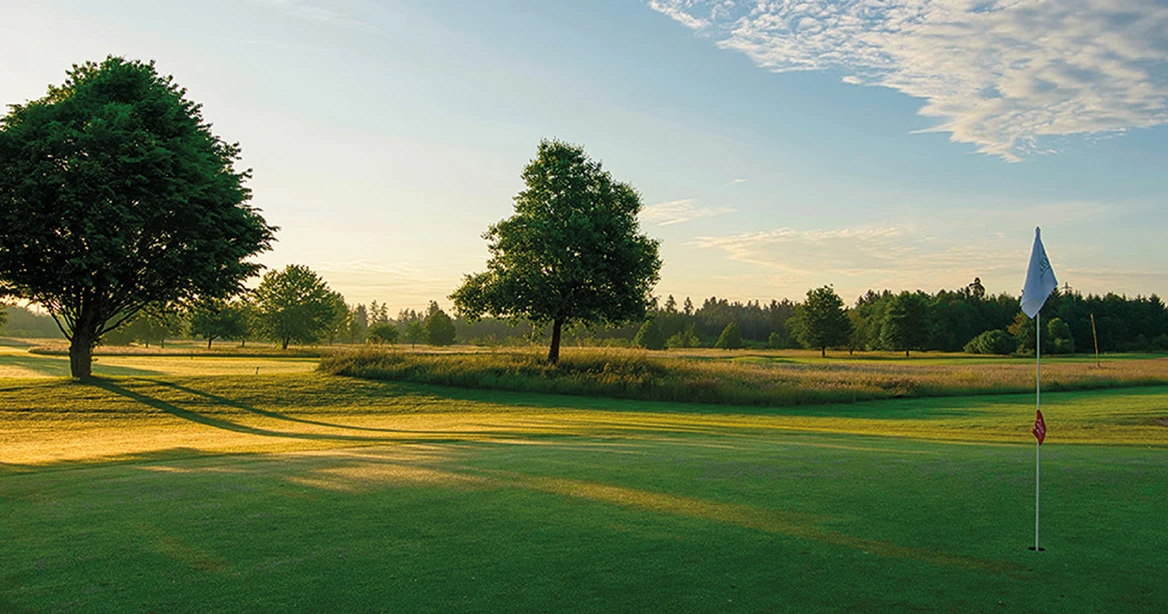 Golfplatz im Morgenlicht mit einer weißen Abschlagsfahne im Vordergrund