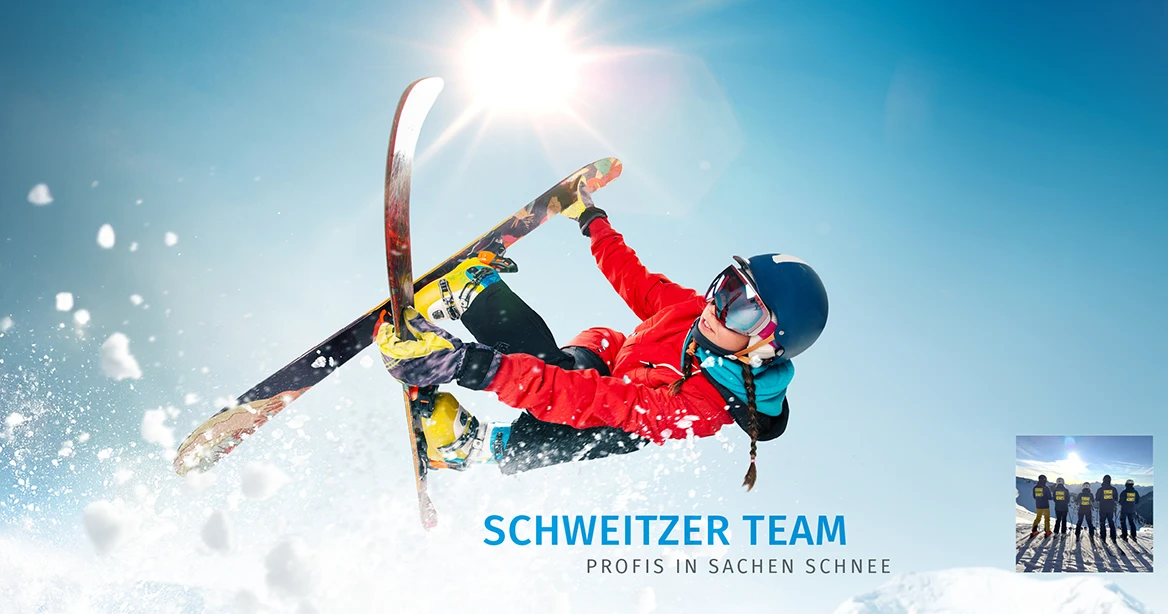 Ein Kind in rotem Skianorak und mit Brille und Helm wirbelt auf gekreuzten Skiern durch die Luft. Der Himmel ist blau, Schneeflocken wirbeln auf.