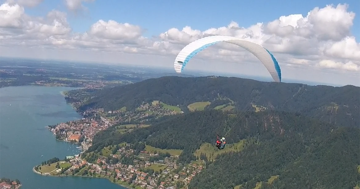 Ein Gleitschirm-Flieger schwebt mit einem weiß-blauen Fallschirm über den Tegernsee.