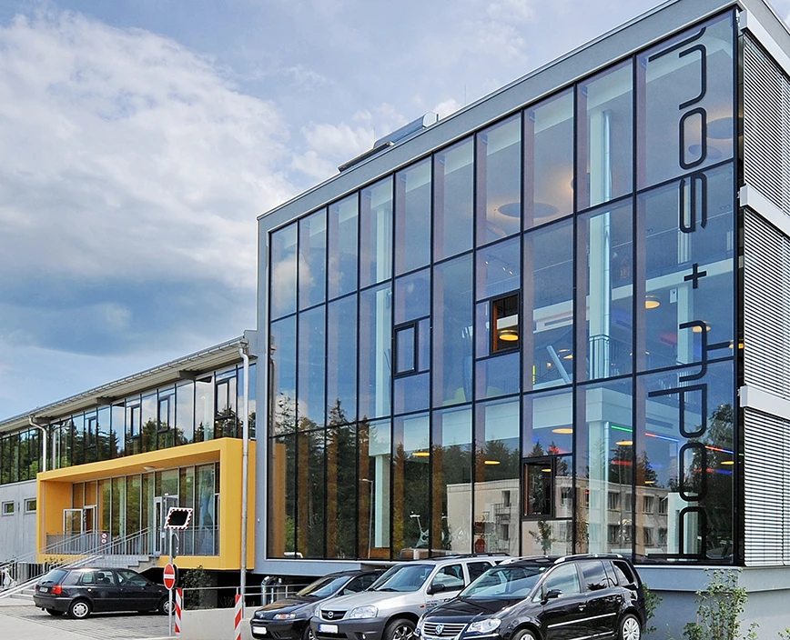 Die Fassade vom Center Brunnthal mit vier paar parkenden Autos vor dem Gebäude.Außenansicht des Centers Brunnthal mit vier vor dem Gebäude geparkten Autos.
