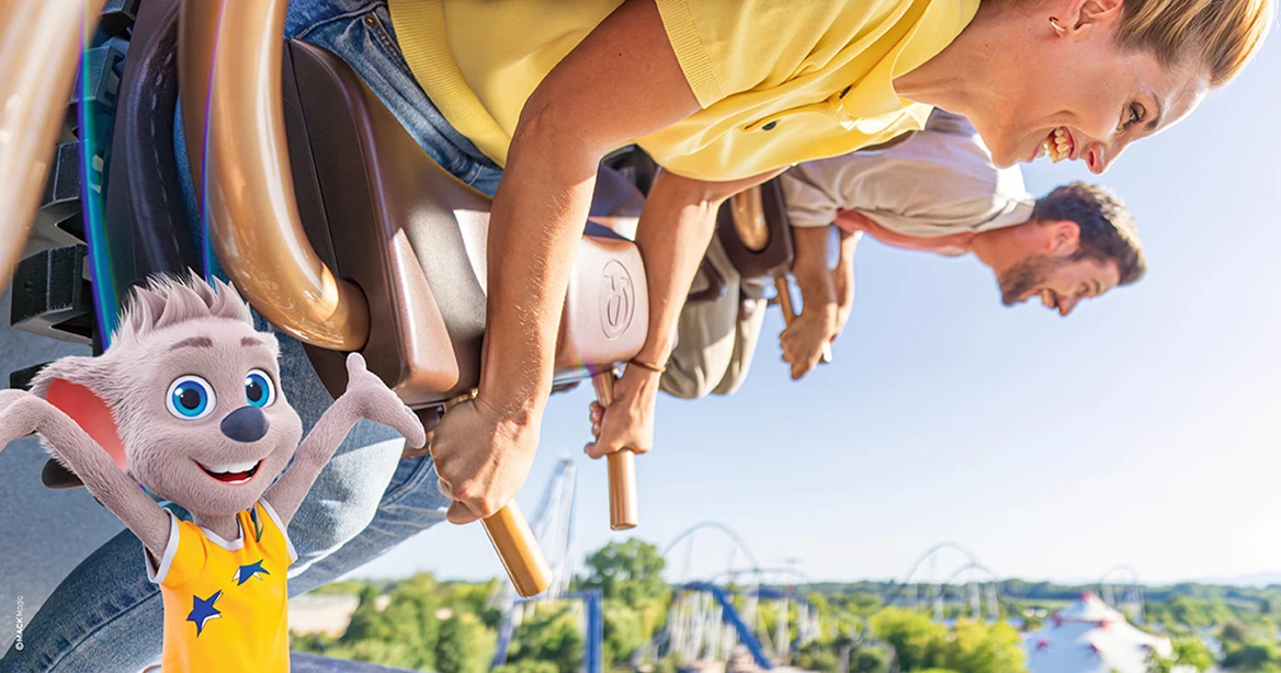 Eine junge Frau und ihr Partner in der Achterbahn im Europa-Park. Die Sonne scheint, beide lachen. Im Vordergrund links sieht man Ed, die Europa-Park Maus.