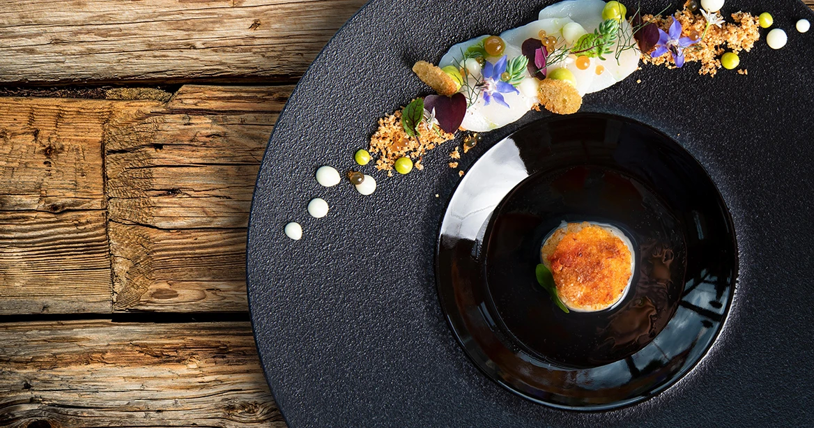 Abbildung einer Speise auf einem schwarzen Teller, dekoriert mit essbaren Blumen, in einem der Hotelrestaurants im Europa-Park.