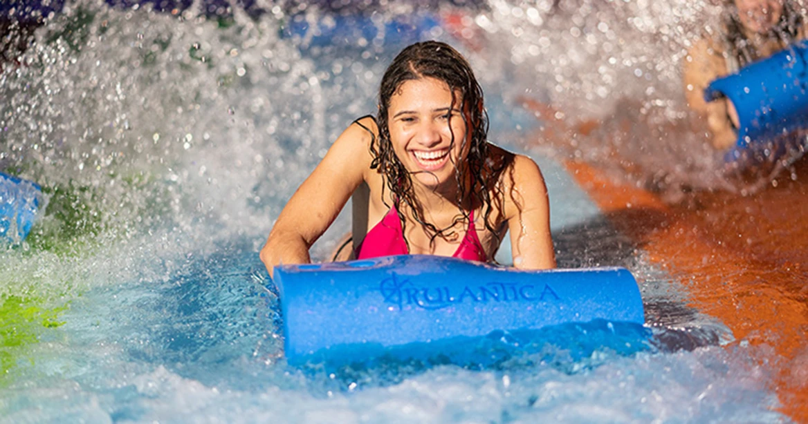 Rulantica Wasserwelt im Europa-Park: Mädchen rutscht auf dem Bauch auf einer Matte eine Wasserrutsche hinunter.
