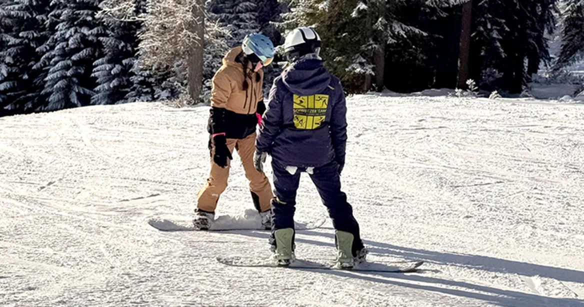 2 Snowboarder auf einem sonnenbeschienenen Übungshang.