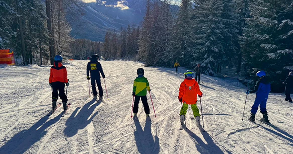 5 Kinder auf Skiern und in bunten Skijacken stehen auf einer Piste nebeneinander.