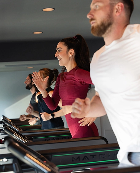 Zwei Frauen und zwei Männer laufen motiviert auf den Laufbändern in einem Fitnessstudio.