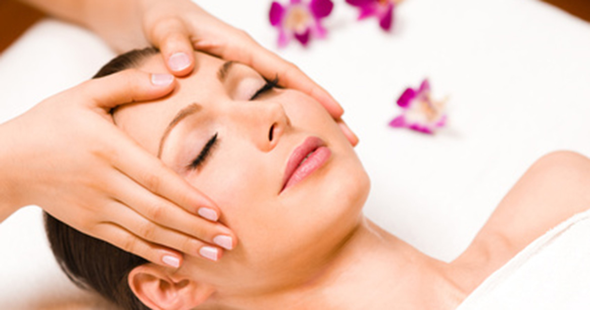 Frau bei Gesichtsmassage mit Blüten im Hintergrund