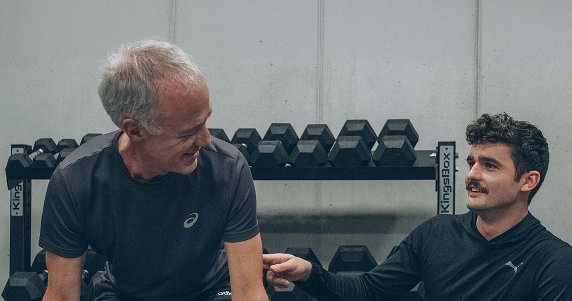 Personal Trainer mit Klient vor Hantelrack