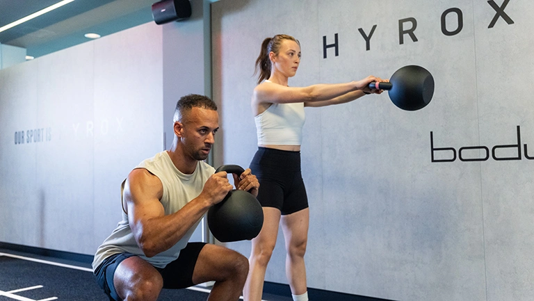Ein Mann und eine Frau beim Kettlebell-Training in der HYROX Area bei body + soul München Mitte.