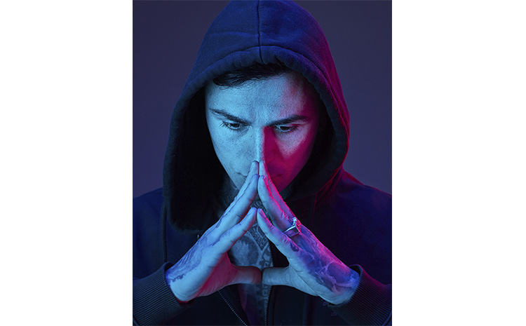 Junger Mann mit Kapuze auf dem Kopf sinniert mit vor dem Mund zusammengelegten Fingerspitzen, im Fotostudio von Deidl und Behnke.