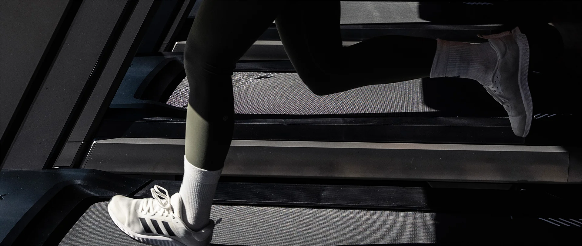 Detailaufnahme einer Frau beim Laufen auf dem Laufband im Fitnessstudio, Fokus auf Beine, Laufschuhe und Bewegung.